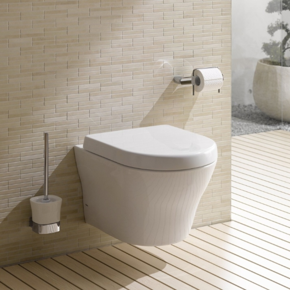 Lifestyle image of the TOTO MH Wall Hung Rimless Toilet installed against a beige wall with toilet roll and toilet brush holder